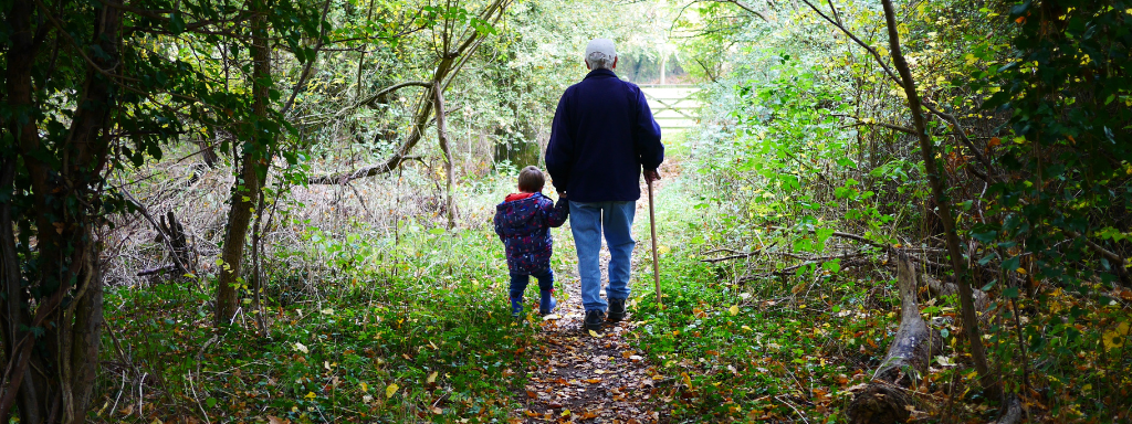 A child holds a grandparent's hand as they walk trough the woods together