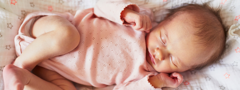 A baby in a pink vest sleeps peacefully