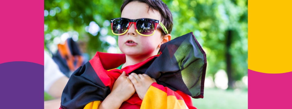 A boy wears sunglasses the colours of the German flag, and has a German flag around his shoulders