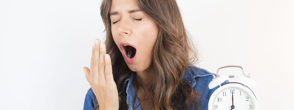 A lady yawns next to her alarm clock