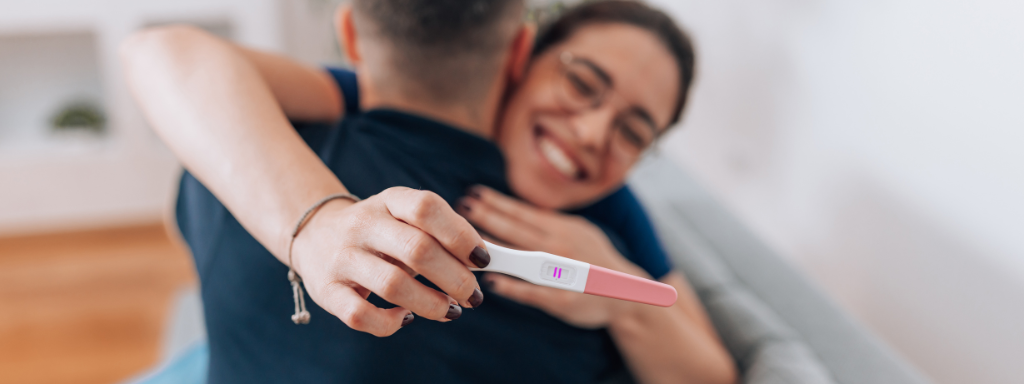 Image shows a woman holding up a pregnancy test while hugging a man