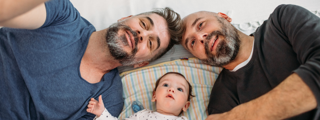 manage intrusive thoughts new parent - the image shows two men and a baby laying on their backs on the floor and smiling at the camera