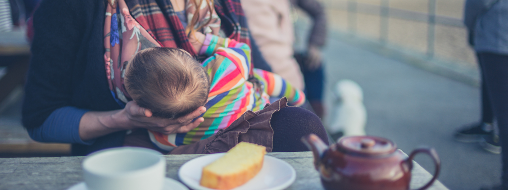 new parent perks and activities - the photo shows a baby lying on a lady's knee in front of a table with teapot, cup and cake on it