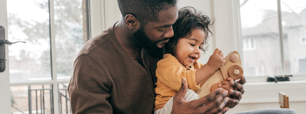 Being an active father to help childhood development - the photo shows a dad holding their child and playing with a wooden toy together